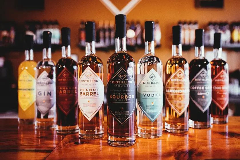 A selection of 477 Distilling spirits in glass bottles on a wooden bar.