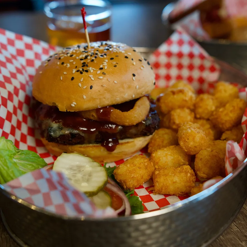 A burger with an onion ring, tater tots and a pickle at The G.O.A.T. Sports Bar.