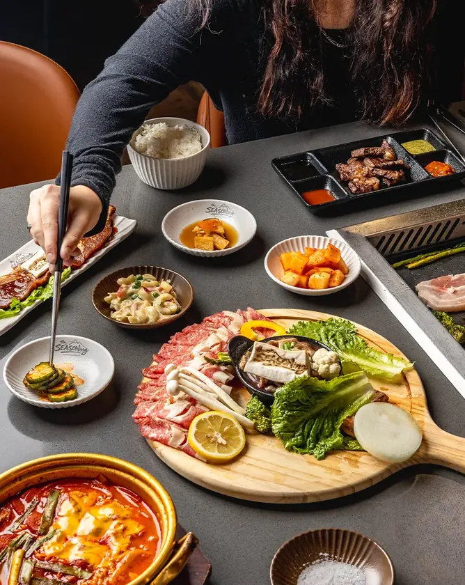 Korean barbecue meats, vegetables and side dishes arranged around a tabletop grill at SEASONing.