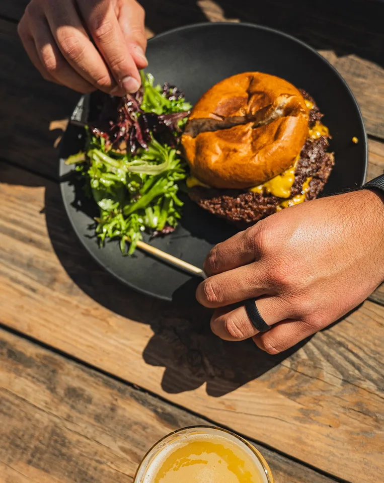 A cheeseburger and green salad with a glass of beer on a patio table at WeldWerks.