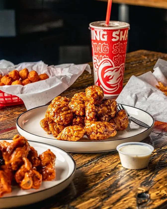 Sauced wings with dipping sauce and a Wing Shack drink on a wooden table.
